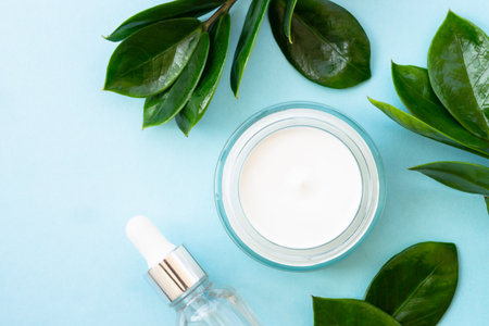 Natural cosmetic, cream jar with green leaves on blue. Flat lay with copy space.の写真素材