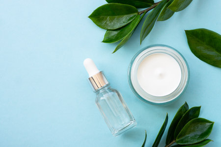 Natural cosmetic, cream jar with green leaves on blue. Flat lay with copy space.の写真素材