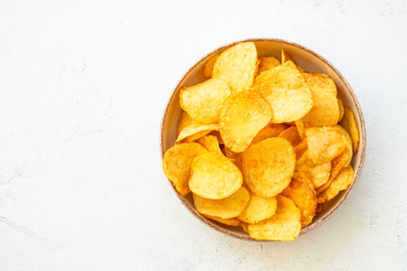 Potato chips in wooden bowl on white table. Top view with copy space.の写真素材