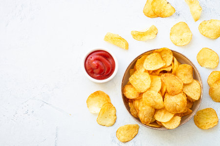 Potato chips in the bowl and ketchup sauce on white table. Top view with copy space.の写真素材