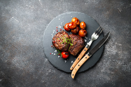 BBQ dish. Meat steaks with vegetables and herbs at black background. Top view image with copy space.の写真素材