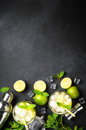 Mojito with rum, lime, mint and ice on black background with bar utensils. Flat lay with copy space.の写真素材