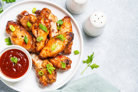 Chicken wings in bbq sauce on craft plate. Top view, close up on white stone table.の写真素材