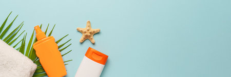 Sunscreen, towel and sunglasses on blue background. Flat lay with copy space, long format.