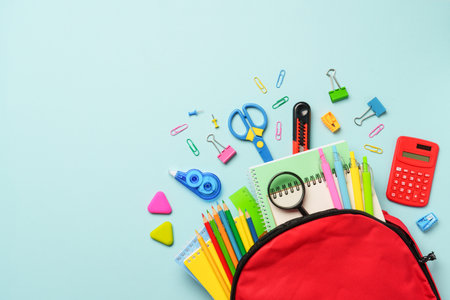 Back to school. School backpack with stationery on blue background. Flat lay with copy space.