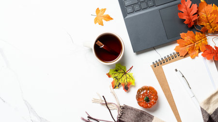Autumn workspace. Laptop, notebook, cup of tea and fallen leaves. Flat lay image with space for...
