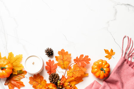 Cozy autumn flat lay background on white. Fallen leaves, scarf and craft candle.