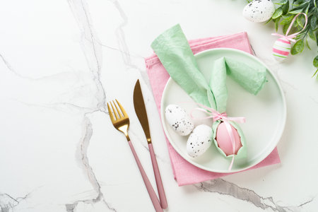 Spring table setting - White plate, golden cutlery and colored easter eggs. Top view with copy...