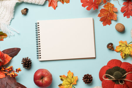 Falling leaves, notepad, knitted scarf and wooden candle on blue background.