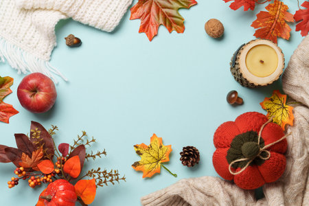 Thanksgiving day background. Knitted sweater, falling leaves and crafted candle on blue background.