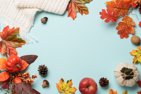 Autumn flat lay background. Knitted sweater, falling leaves and crafted candle on blue background.