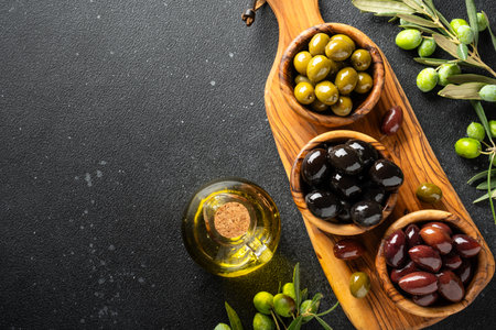 Olives mix and Olive oil with fresh olive tree branches. Top view on black table with copy space.の写真素材