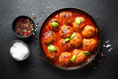Glazed Meatballs in tomato sauce in iron plate on black background. Top view with space for text.の写真素材