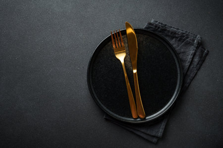 Black plate with golden cutlery at black. Flat lay with copy space.