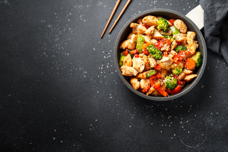Chicken stir fry with vegetables and sesame at black background. Top view with copy space.の写真素材