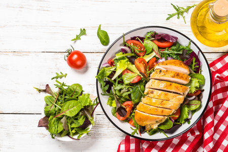 Green salad with baked chicken breast at white kitchen table. Healthy food, clean eating concept. Top view image.の写真素材