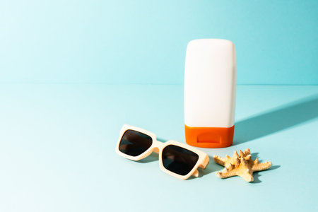 Summer background. Sunglasses, sunscreen and sea shell with sunny shadows. Trendy summer concept.