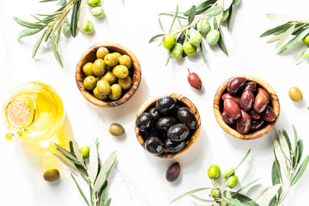 Olives in wooden bowls and Olive oil in the bottle at white table with copy space.