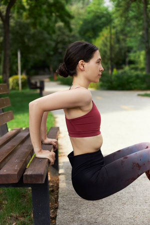 Young smiling woman doing push-ups on bench outdoors