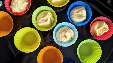 Top view of colorful silicone cupcake liners partially filled with raw muffin batter, ready to be...