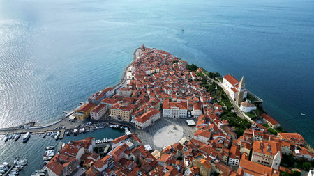 Stunning aerial view of Piran old town in Slovenia with red rooftops, St. Georges church, harbor, and the blue Adriatic Sea under bright sunlightの写真素材