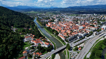 Beautiful panoramic aerial view of a historic European city with red rooftops, flowing river, green hills, and distant mountains under a bright skyの写真素材