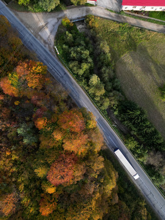 Aerial view of mountain road with truck passing through colorful autumn forest
