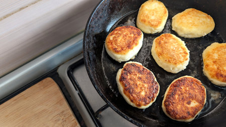Golden cottage cheese pancakes frying in skillet during homemade breakfast cooking