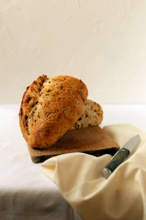 Fresh bread on a light background on the table. Sliced up on the board. Nearby a knife and a napkinの写真素材