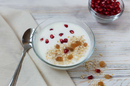Yogurt with muesli and fruit for breakfast in a bowl, pomegranate seeds in a bowl, white wooden background, flat lay, copy spaceの写真素材