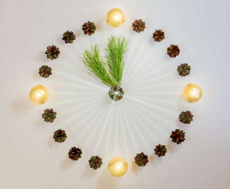 Original new year clock made of balls and cones with rays, pine branches instead of arrows, flat lay, copy space, light backgroundの写真素材