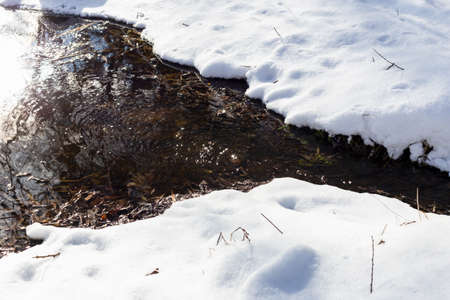 A stream makes its way through the snow, sparkling in the sun. Joy of life, thaw, hopeの写真素材