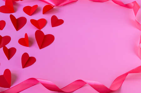 Soaring red hearts on a pink background framed by a satin ribbon. Valentines Day. The perfect solution for your design on the theme of love. Top view, copy space, selective focusの写真素材