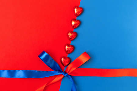 Red hearts on a red-blRed hearts lie diagonally on a red and blue background with a bow of satin ribbons. Valentines Day. Flat lay, copy space, space for textue background with a bow of satin ribbonsの写真素材