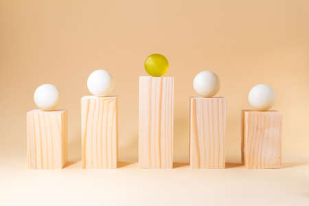 Prominent yellow sphere among white spheres on wooden bars on pastel beige background. Difference in...