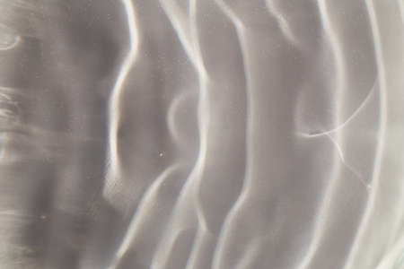 Gray-White textured background of waves on water in sunlight. Close-up, selective focus