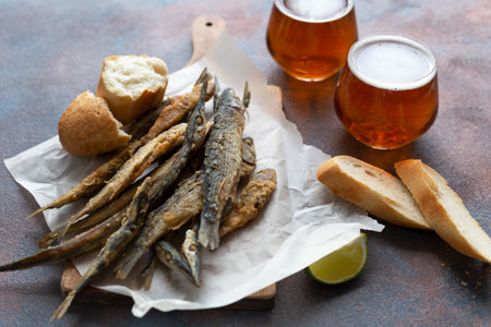 Fried fish on a board with a sheet of parchment surrounded by beer, bread and lime. Still life. Top viewの写真素材