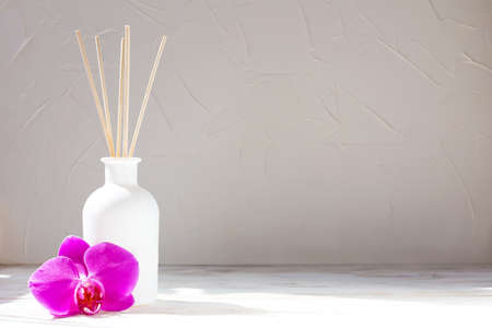 Perfume for the home. Aromatic reed diffuser on a light background with orchid flower. The concept...