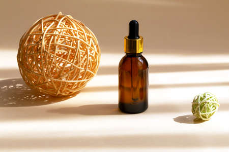 Brown glass bottle with dropper between large yellow and small green wicker rattan spheres. Organic, natural cosmetics. Beauty, skin care. SPA products. Close-up, copy space. Selective focusの写真素材