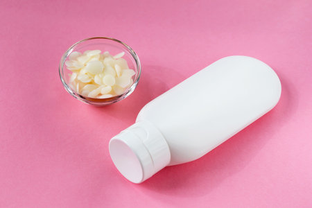 On a pink background is a white cosmetic tube. Nearby in a glass bowl is beeswax. Cosmetics, cosmetology, careの写真素材