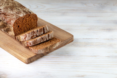 Loaf of dark bread with slices on a board on a white wooden background