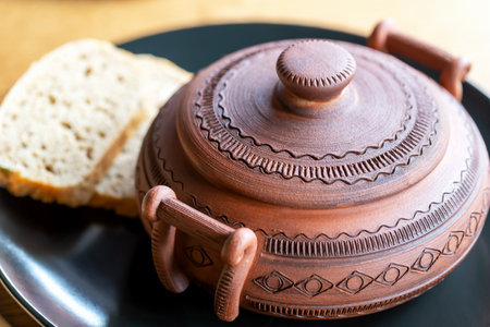 Pot of hot soup and two pieces of bread on black plate. Serving in restaurant. Selective focus, defocusの写真素材