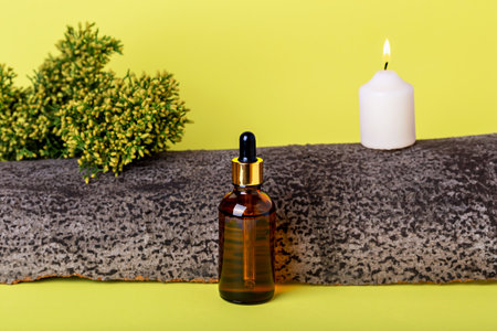 Glass cosmetic amber bottle, plant, burning candle and tree bark on yellow background. Organic cosmetics. Natural careの写真素材