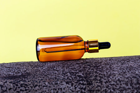 Glass cosmetic amber bottle lying on bark tree on yellow background. Organic cosmetics. Natural careの写真素材