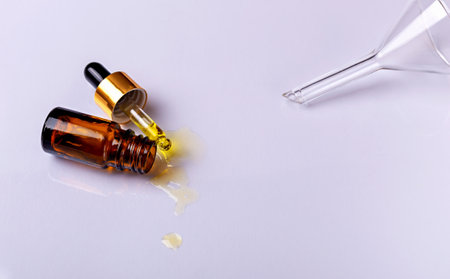Laboratory studies. Dropper with drops of yellow liquid and glass amber cosmetic bottle on white background. Laboratory glass funnel. Natural organic cosmetics. Selective focusの写真素材