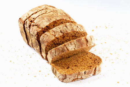 Sliced fresh baked loaf of dark delicious bread with crumbs on white background