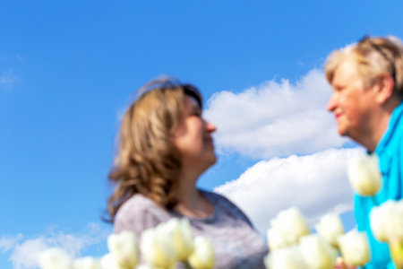 An elderly mother and young daughter look at each other against clear sky. Family relations. Selective focus, defocus, blurの写真素材
