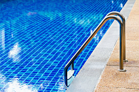 Bright blue tiled swimming pool with stainless steel ladder, leading into water, creating refreshing...