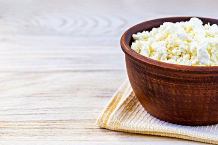 Closeup fresh cottage cheese served in rustic ceramic bowl on light napkin on wooden background. Ideal for healthy dietの写真素材