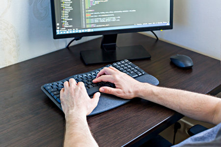 Close-up view of male hands typing on keyboard, emphasizing precision in software coding in modern home office settingの写真素材